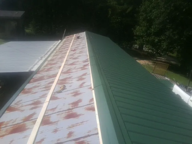 Old rusted panels beside newly installed green metal roofing — Wind Damage Roof Repair by Roofing Brothers in Arkadelphia