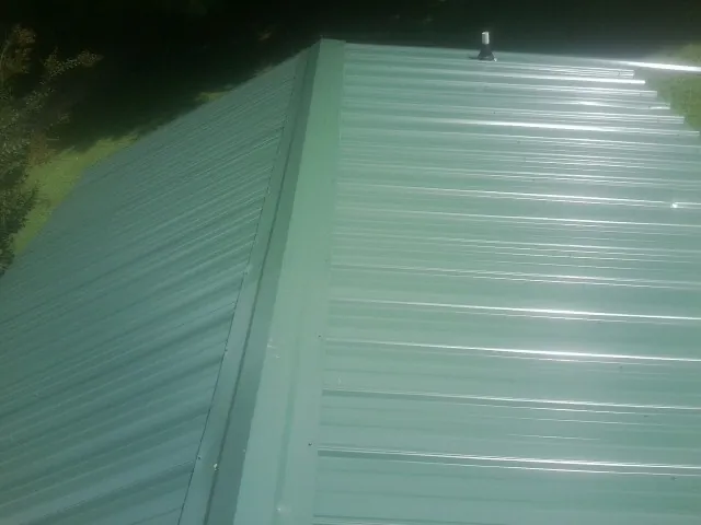 New green metal panels meeting at the ridge of a roof — Flat Roof Repair work by our crew in Arkadelphia