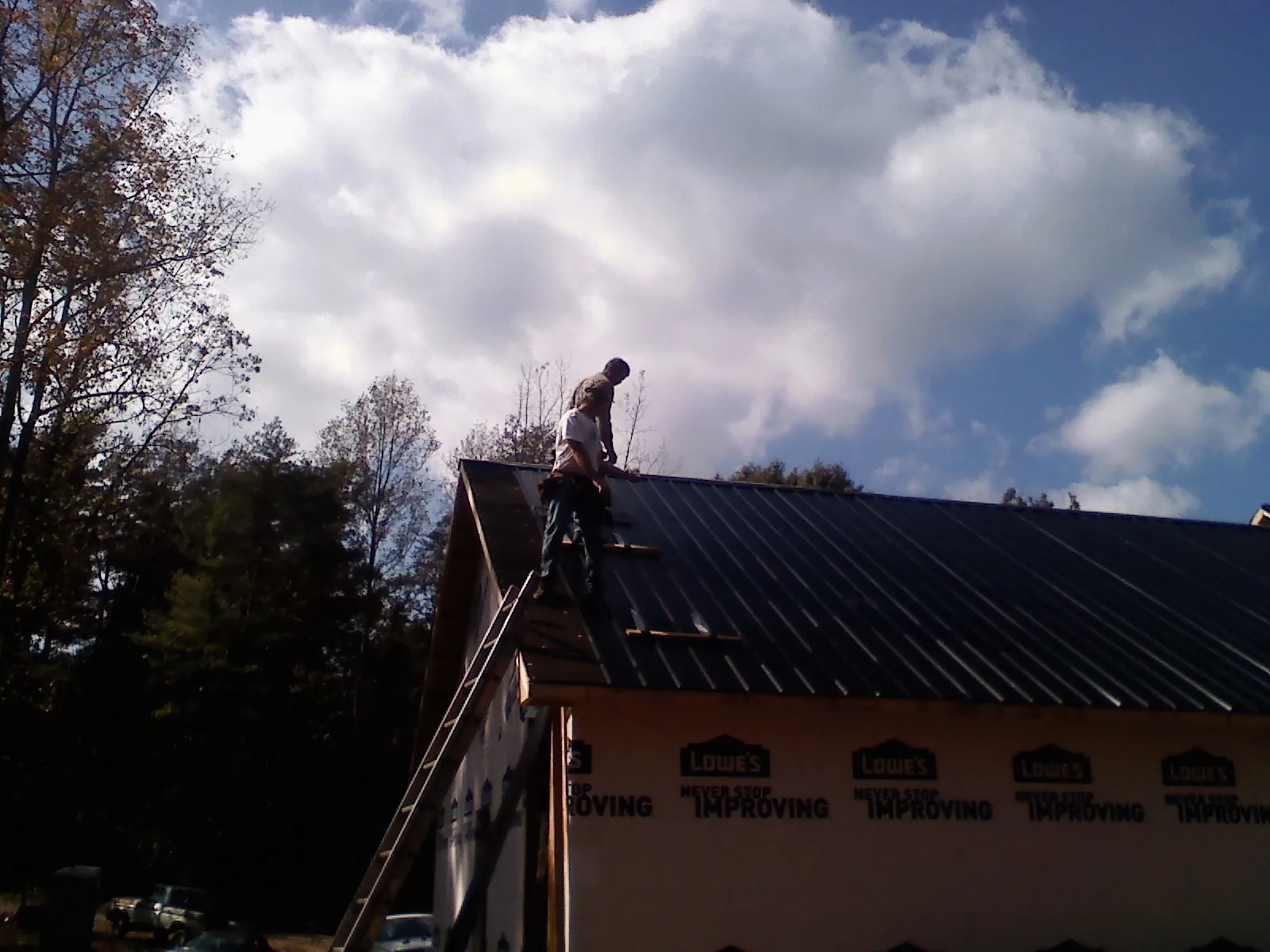 Roofer fastening dark metal panels high against a cloudy sky, from a Roof Inspection job in Arkadelphia