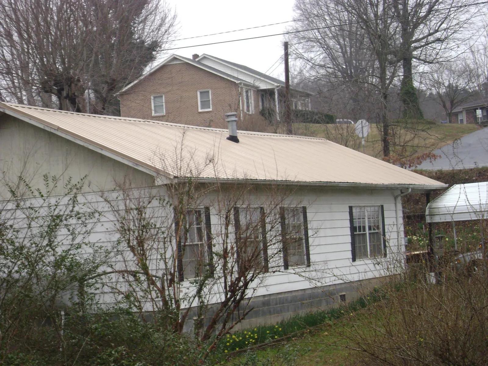 Tan metal roof on a white sided house set into a hillside — Commercial Roofing by Roofing Brothers in Arkadelphia