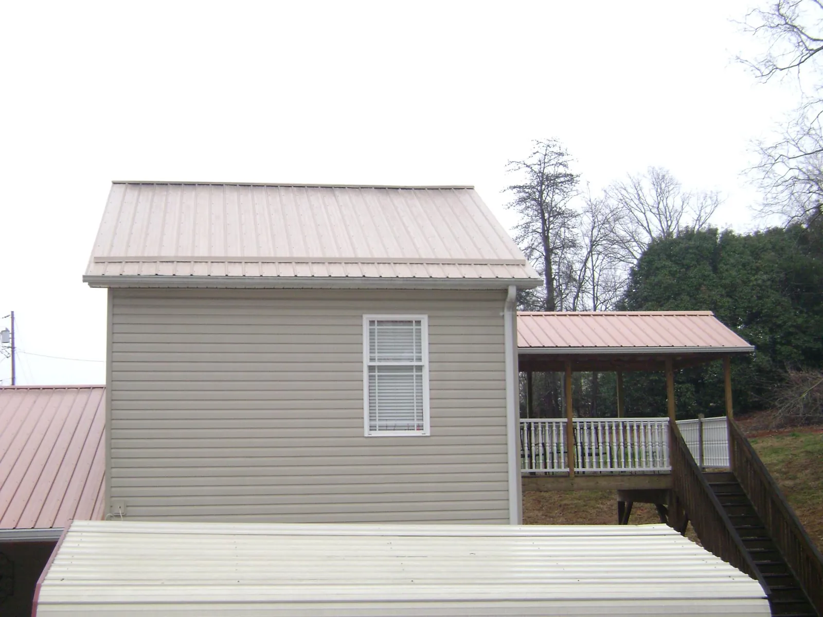 Tan metal roofs on a two story addition and attached porch, from a Roof Replacement job in Arkadelphia